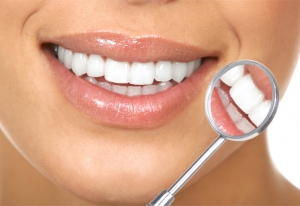 person showing healthy white teeth, checking them with a dental mirror